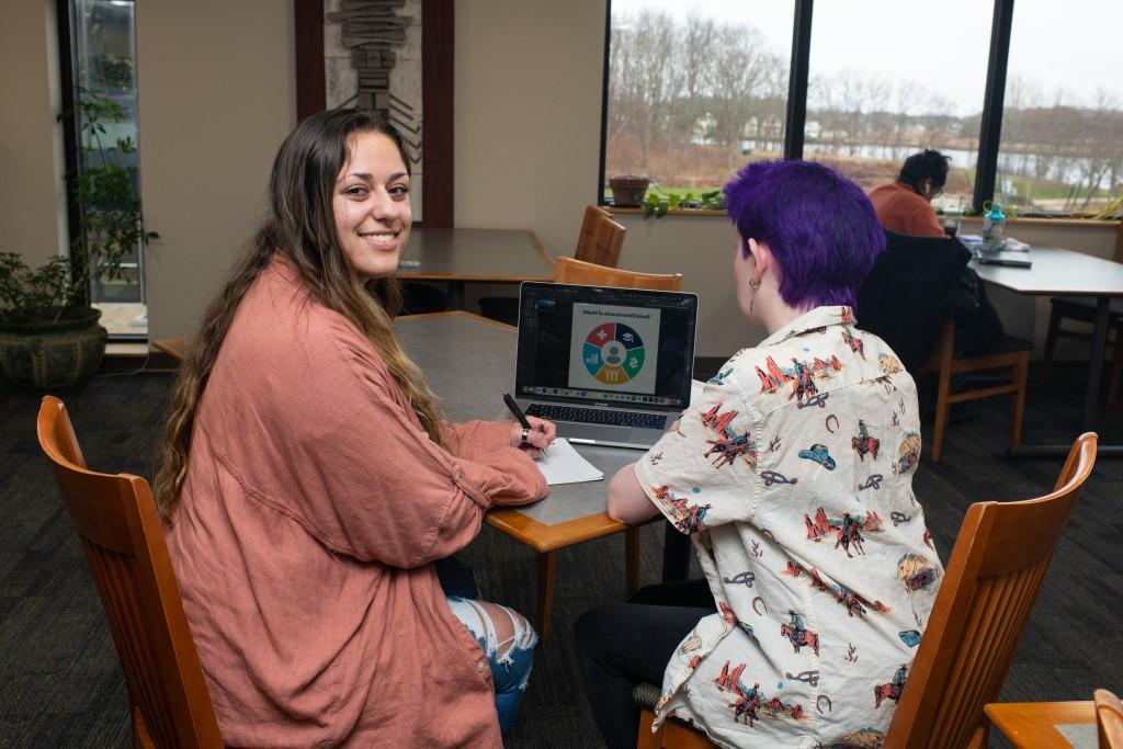 Two students study at a table with a lap top