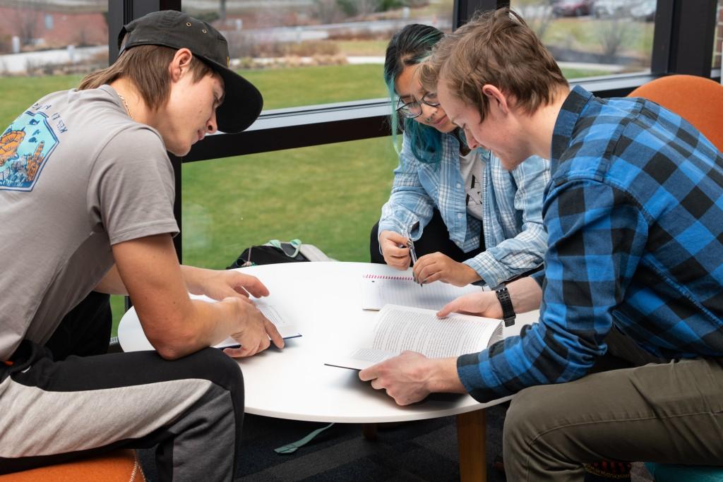 Three U N E students gather around a table studying notes