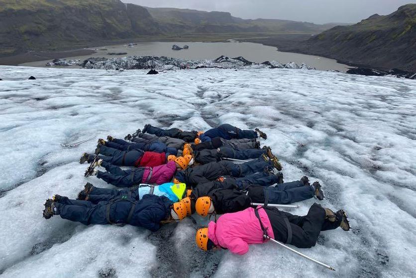 一群学生穿着冬装，戴着安全帽，躺在室外的冰湖上