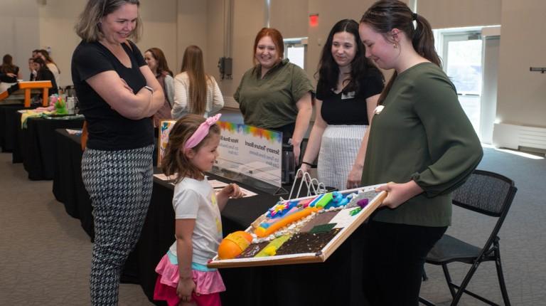 在自闭症博览会上，一群学生和一个小女孩分享一个感官纹理板