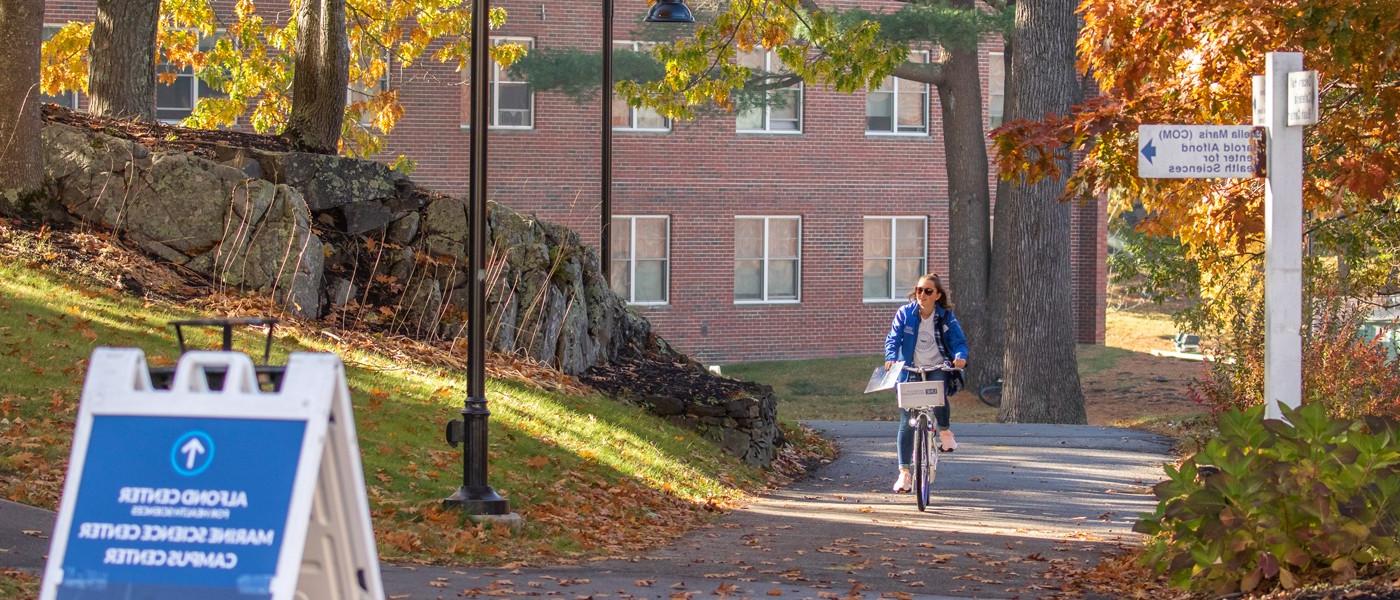 a student rides a bicycle through the biddeford campus in the fall